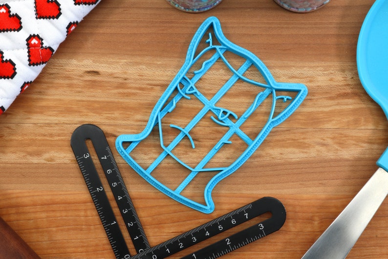 May include: A blue plastic cookie cutter shaped like a dog's head. The cutter has a detailed design with lines and curves.