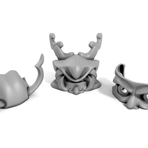 May include: Three gray plastic masks with different designs. The masks are all in the shape of a face, with different features such as horns, teeth, and eyes.