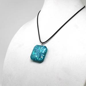 May include: A turquoise blue pendant necklace with a square-shaped pendant with iridescent glitter embedded in the resin. The pendant is hanging from a black cord.