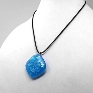 May include: A blue resin pendant with a white design hangs from a black cord necklace.