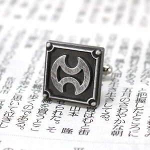 May include: Silver cufflinks with a black and silver design. The design features a stylised symbol with two overlapping circles.