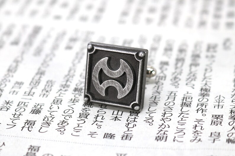May include: Silver cufflinks with a black and silver design. The design features a stylised symbol with two overlapping circles.