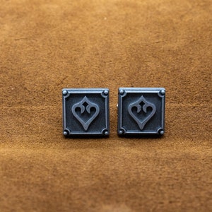 May include: Two silver cufflinks with a square design and a stylized heart in the center.