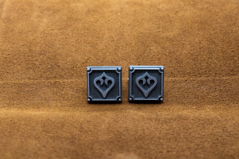 May include: Two silver cufflinks with a square design and a stylized heart in the center.