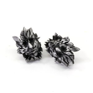 Pu&ograve; includere: Un paio di orecchini d'argento con un design a forma di viso. Gli orecchini sono realizzati con molte piccole forme geometriche che creano un aspetto testurizzato e astratto.