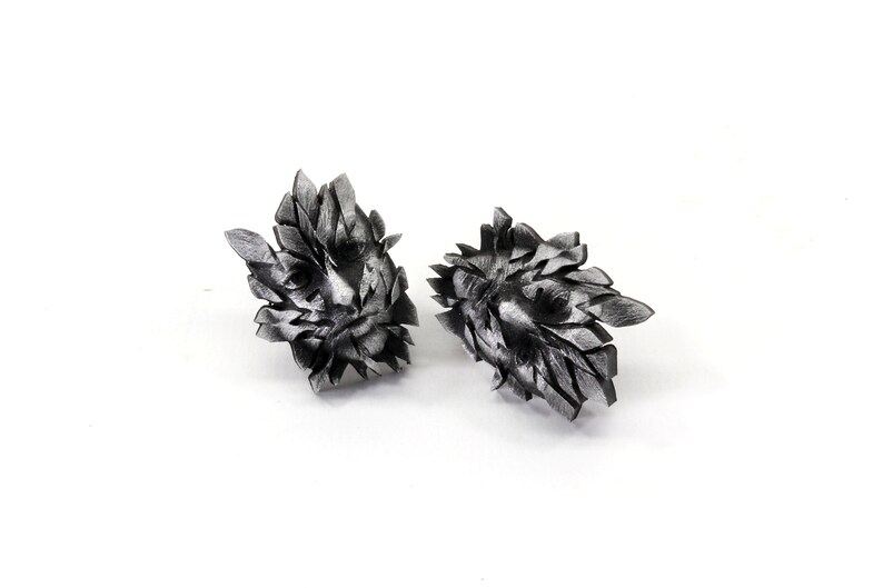 Pu&ograve; includere: Un paio di orecchini d'argento con un design a forma di viso. Gli orecchini sono realizzati con molte piccole forme geometriche che creano un aspetto testurizzato e astratto.