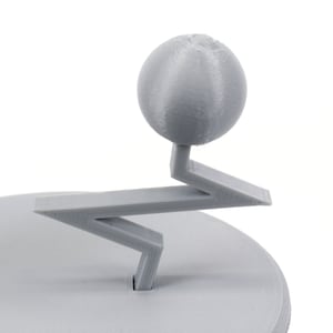 Pode incluir: Um modelo 3D impresso em cinza de um planeta em um suporte. O planeta &eacute; uma esfera com uma superf&iacute;cie texturizada. O suporte tem a forma de um ziguezague com uma base circular.