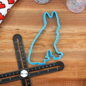 May include: Blue plastic cookie cutter shaped like a German Shepherd dog silhouette. The cutter is on a wooden surface with a ruler and other baking supplies.