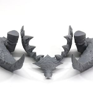 May include: A set of three gray 3D printed dinosaur jaws. The jaws are separated into three pieces: the upper jaw, the lower jaw, and the teeth. The jaws are detailed with sharp teeth and textured scales.