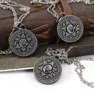 May include: Three silver-tone pendant necklaces with a circular design featuring text and a central starburst image. The necklaces are displayed on a leather surface with a metal tool in the background.