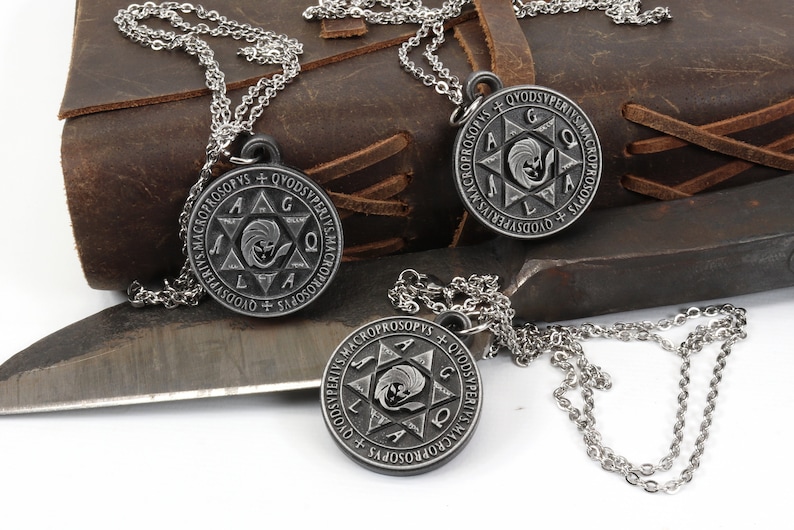 May include: Three silver-tone pendant necklaces with a circular design featuring text and a central starburst image. The necklaces are displayed on a leather surface with a metal tool in the background.