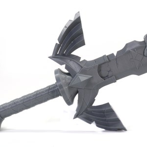 May include: A gray plastic model of the Master Sword from the Legend of Zelda video game series. The sword has a detailed design with a handle, a blade, and a hilt with a triangular shape.