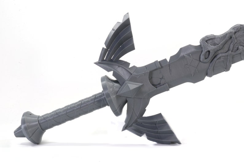 May include: A gray plastic model of the Master Sword from the Legend of Zelda video game series. The sword has a detailed design with a handle, a blade, and a hilt with a triangular shape.
