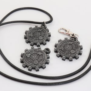 May include: Two silver-colored pendants with intricate designs, one on a black cord necklace and the other on a black cord keychain.