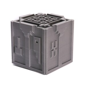 May include: A gray 3D printed cube with a grid pattern on the top and a design on each side. The design on the front side is a stylized letter "H".