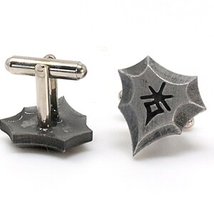 May include: A pair of silver cufflinks with a geometric design. The cufflinks feature a black kanji character in the center.