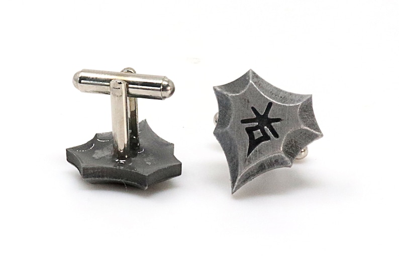 May include: A pair of silver cufflinks with a geometric design. The cufflinks feature a black kanji character in the center.