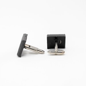 May include: A pair of gray concrete cufflinks with silver metal clasps.