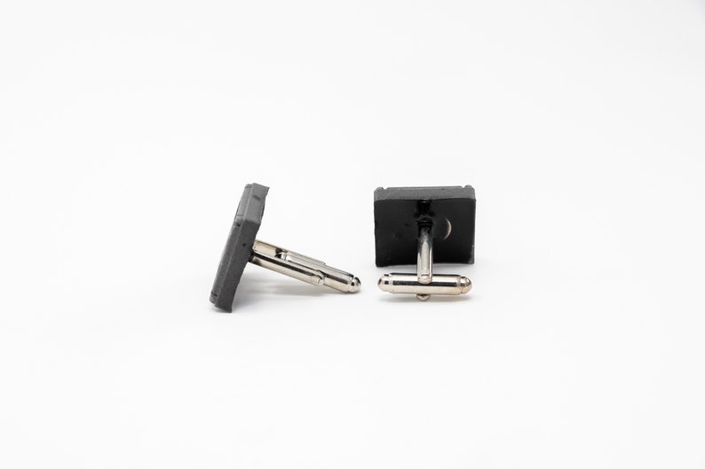 May include: A pair of gray concrete cufflinks with silver metal clasps.
