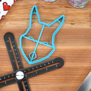 May include: A blue plastic cookie cutter shaped like a dog's head. The cutter is on a wooden surface with a black ruler.