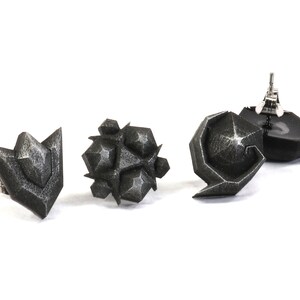 May include: Three black geometric earrings with a textured finish. The earrings are in the shape of a point, a cluster of points, and a curved shape.