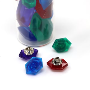 May include: Four colorful plastic gem pins with silver backs. The gems are blue, green, red, and purple.