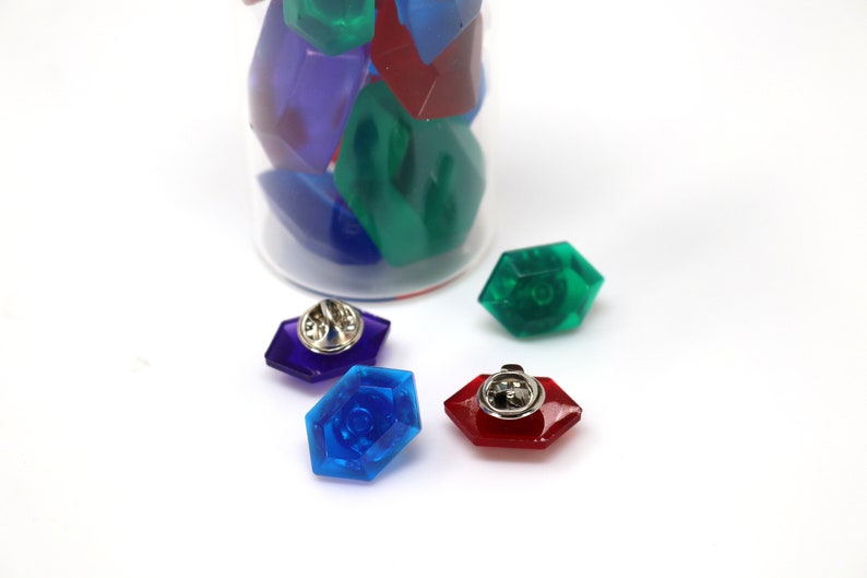 May include: Four colorful plastic gem pins with silver backs. The gems are blue, green, red, and purple.