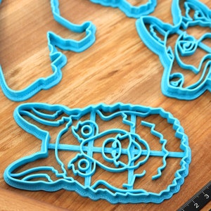 May include: A set of four blue plastic cookie cutters shaped like animal faces. The cutters are on a wooden surface.