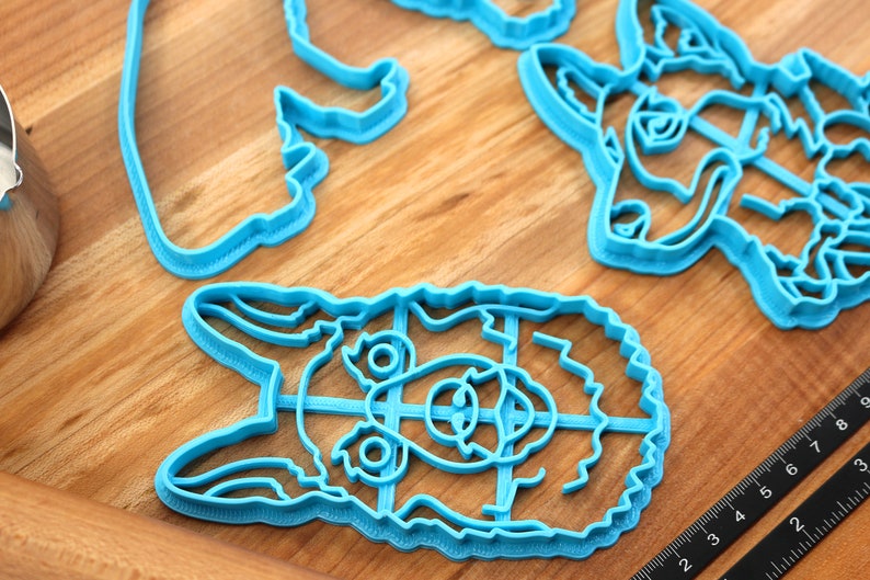 May include: A set of four blue plastic cookie cutters shaped like animal faces. The cutters are on a wooden surface.