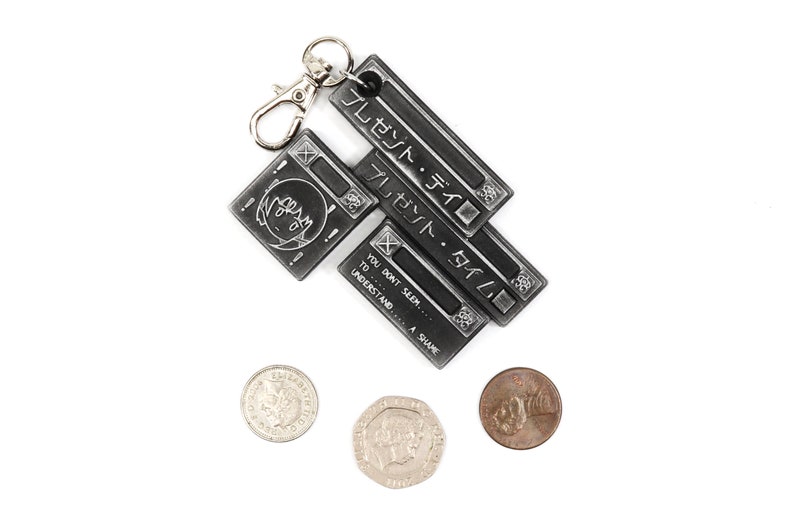 May include: A silver keychain with three metal tags. The top tag says "プレゼント・タイム" in Japanese. The middle tag says "プレゼント・タイム" in Japanese. The bottom tag says "YOU DON'T SEEM... TO... UNDERSTAND... A SHAME".