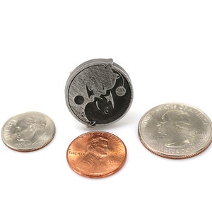 May include: A silver yin yang pendant with a black and white design. The pendant is shown next to three US coins: a quarter, a dime, and a penny.
