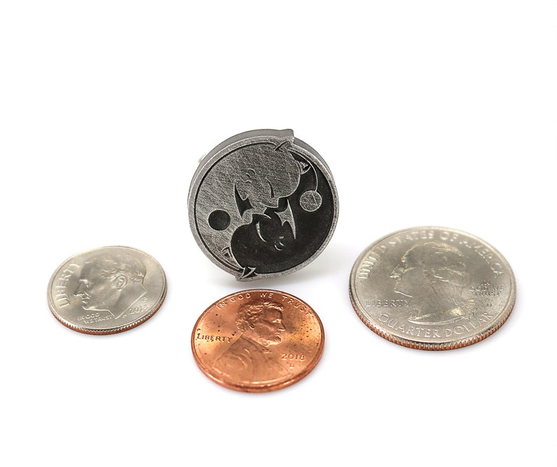 May include: A silver yin yang pendant with a black and white design. The pendant is shown next to three US coins: a quarter, a dime, and a penny.