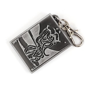 May include: A silver metal keychain with a black and white image of a creature with tentacles. The keychain has a silver metal clasp.