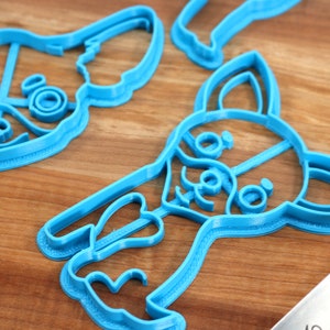 Puede incluir: Tres cortadores de galletas de pl&aacute;stico azul con forma de perro chihuahua. Los cortadores est&aacute;n sobre una superficie de madera.