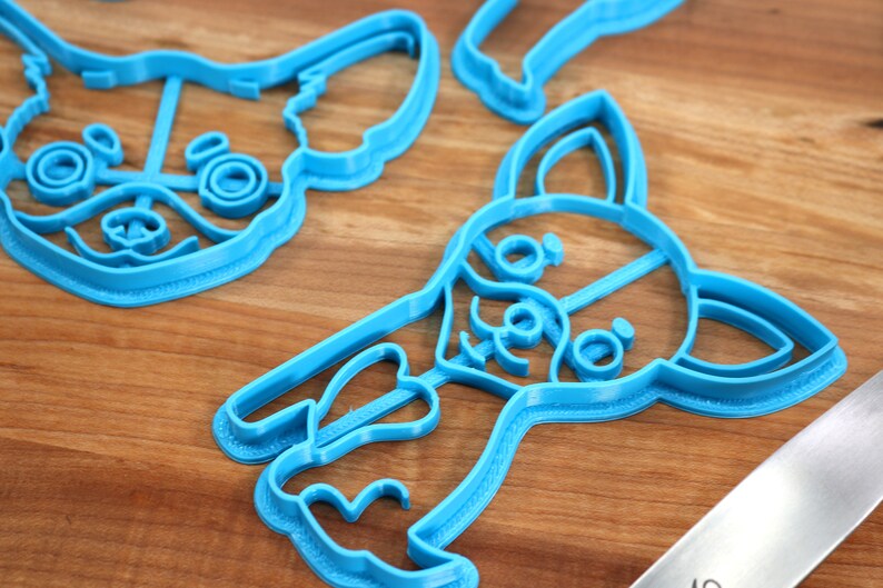 Puede incluir: Tres cortadores de galletas de pl&aacute;stico azul con forma de perro chihuahua. Los cortadores est&aacute;n sobre una superficie de madera.