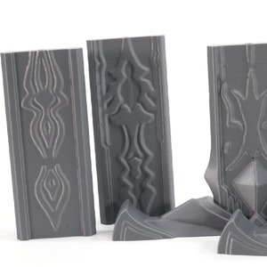 May include: Four gray 3D printed wall panels with intricate geometric designs. The panels are made of a smooth, matte plastic and have a slightly textured surface. The designs on the panels are reminiscent of ancient architecture or tribal art.