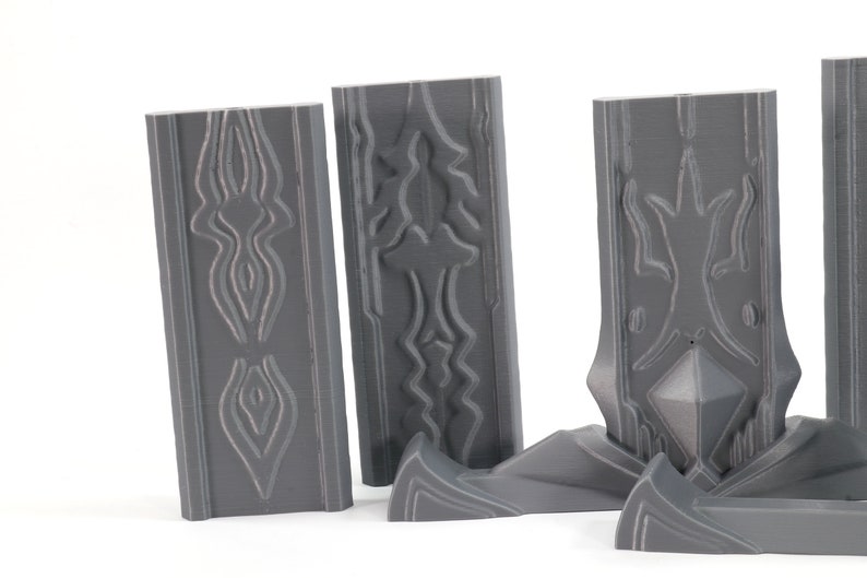 May include: Four gray 3D printed wall panels with intricate geometric designs. The panels are made of a smooth, matte plastic and have a slightly textured surface. The designs on the panels are reminiscent of ancient architecture or tribal art.
