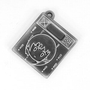 May include: A silver-toned metal charm with a cartoon face and exclamation points around the edge. The charm has a small loop at the top for attaching to a necklace or bracelet.