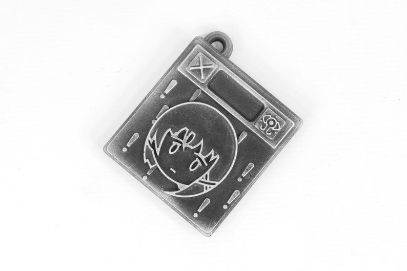 May include: A silver-toned metal charm with a cartoon face and exclamation points around the edge. The charm has a small loop at the top for attaching to a necklace or bracelet.