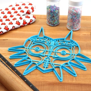 May include: A blue plastic cookie cutter shaped like the iconic Legend of Zelda Majora's Mask. The cutter is on a wooden surface with a rolling pin, a ruler, and two jars of sprinkles.
