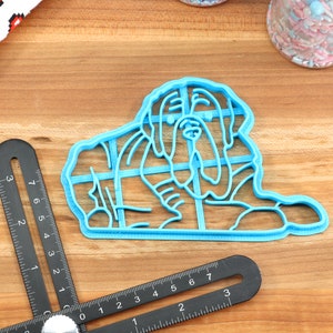 Peut inclure: Un emporte-pi&egrave;ce en plastique bleu en forme de chien, pos&eacute; sur une surface en bois.