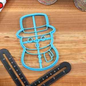 Op de afbeelding: Blauwe plastic sneeuwman koekjesvormer met een hoed, ogen, neus en sjaal.