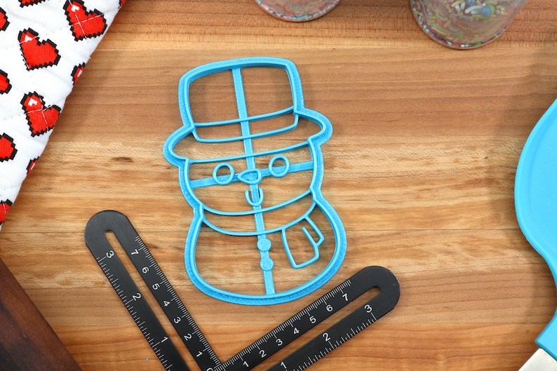 Op de afbeelding: Blauwe plastic sneeuwman koekjesvormer met een hoed, ogen, neus en sjaal.