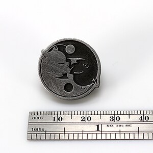 May include: A silver-toned yin yang pin with a black and white design of two dragons facing each other. The pin is approximately 2 cm in diameter.