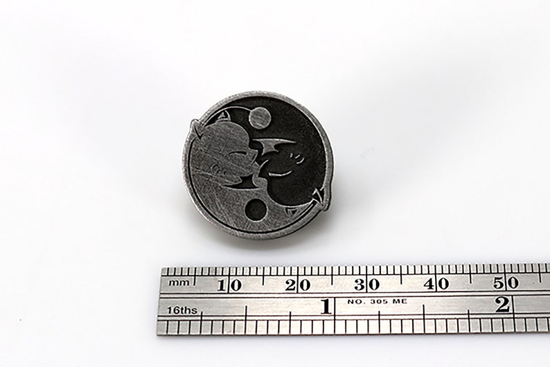 May include: A silver-toned yin yang pin with a black and white design of two dragons facing each other. The pin is approximately 2 cm in diameter.