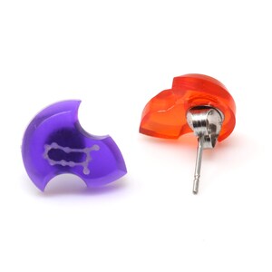 May include: A pair of earrings, one purple and one orange, with a silver post. The purple earring has a Gemini zodiac symbol.