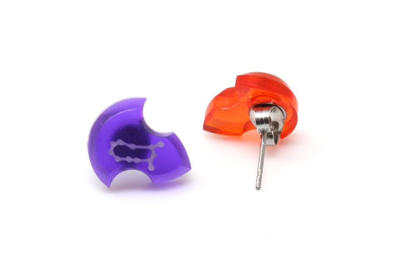 May include: A pair of earrings, one purple and one orange, with a silver post. The purple earring has a Gemini zodiac symbol.