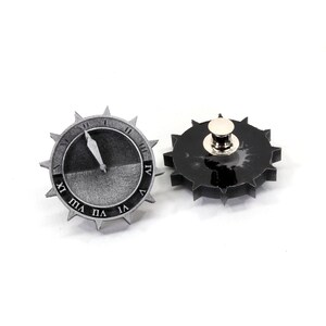 Puede incluir: Dos pines de metal plateados en forma de esferas de reloj con n&uacute;meros romanos. Un pin tiene una esfera negra y el otro tiene una esfera blanca con una aguja negra.