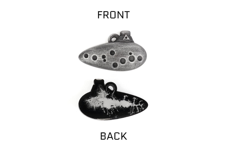 Puede incluir: Un colgante de ocarina plateado con un dise&ntilde;o triangular en la parte superior y una serie de agujeros en la parte delantera. La parte posterior del colgante es negra con un dise&ntilde;o blanco.