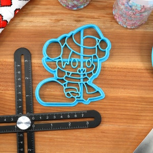 May include: A blue plastic cookie cutter shaped like a cartoon character wearing a Santa hat and holding a snowball. The character has a red nose and big eyes.